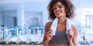 Mulher sorrindo na academia com uma toalha em volta do pescoço