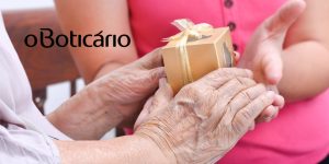 Pessoa idosa recebendo um presente; no lado esquerdo, a logomarca do Boticário