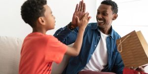 Homem negro recebendo um presente do filho pequeno; os dois celebram