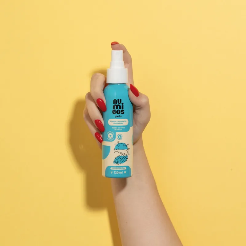Uma mão feminina segurando um frasco de Limpa e Hidrata Patinhas Au.Migos Pets