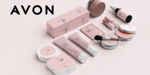 Cosméticos variados dispostos em uma superfície plana; ao lado, a logo da Avon