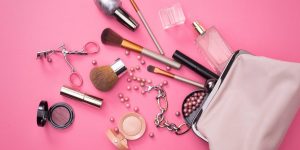 Itens de maquiagem diversos espalhados sobre uma superfície rosa