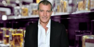Antonio Banderas em destaque em uma montagem que tem uma prateleira de perfumes ao fundo