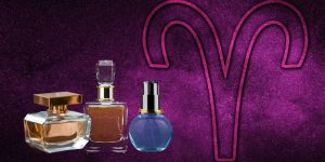 Frascos de perfumes enfileirados e uma arte com o símbolo do signo de áries ao fundo